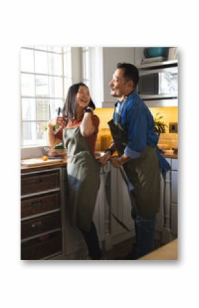 Mature couple in kitchen laughing and preparing meal together, wearing aprons