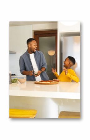 Father and son laughing while preparing pizza together in modern kitchen
