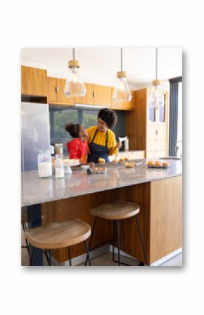 Decorating Diverse mother and daughter working on kitchen island, with cupcakes and pastry bag
