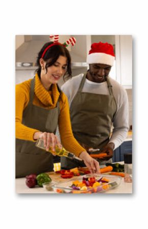 Multiracial couple in festive hats preparing holiday meal together in kitchen, at home