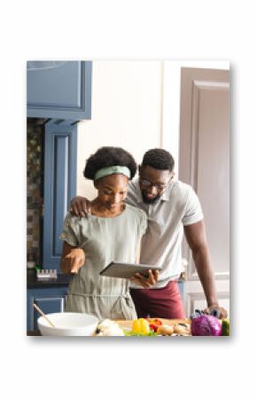Happy african american couple preparing meal together using tablet in kitchen, copy space