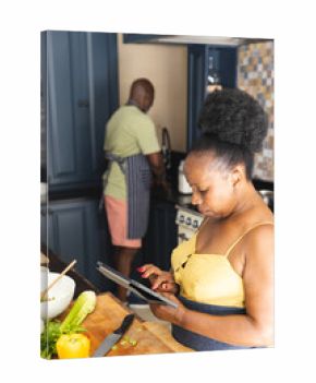 Focused senior african american couple preparing meal together, using tablet in kitchen