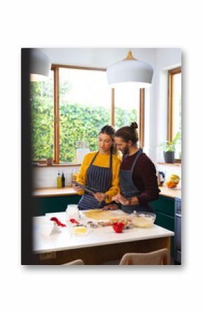 Focused caucasian couple preparing dough, baking cookies and using tablet in kitchen, copy space