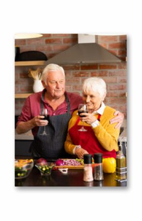 Happy caucasian senior couple preparing vegetables, drinking wine, embracing in kitchen, copy space