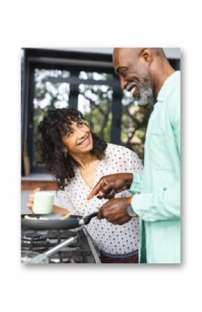 Happy mature diverse couple making breakfast and having coffee in sunny kitchen