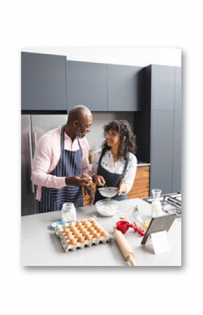 Happy mature diverse couple preparing baking mix using tablet in sunny kitchen, copy space