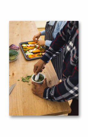 Midsection of diverse senior couple preparing healthy meal with vegetables in kitchen