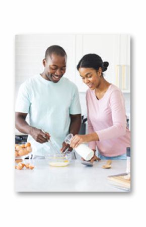 A diverse couple is preparing a meal together, making eggs, in a bright kitchen at home