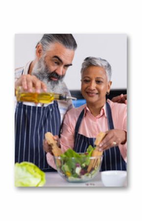 Senior couple preparing salad together, pouring olive oil and mixing ingredients