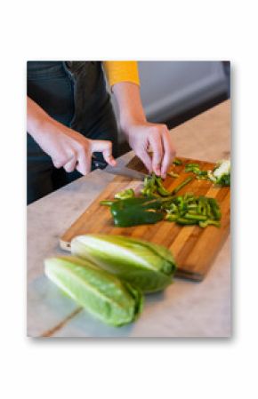 Chopping green bell peppers on cutting board, person preparing fresh vegetables