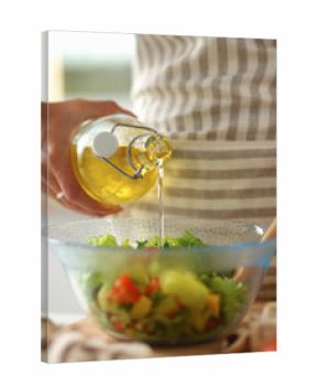 Smiling young woman  mixing fresh salad, holding bottle of oil