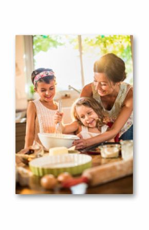 A mother is cooking a cake with her two young daughters