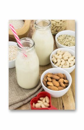 Bottles of homemade plant based milk and bowls with ingredients, on wooden background