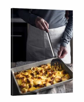 Cutting tartiflette in the baking tray  on the wooden table