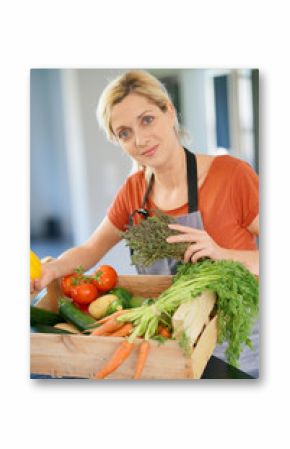 Portrait of woman in domestic kitchen holding basket of fresh vegetables