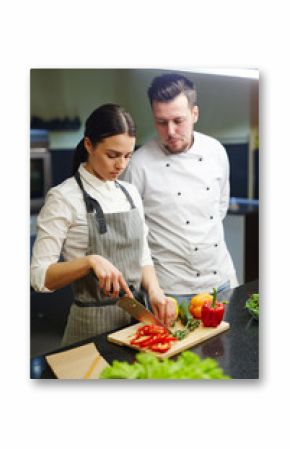 Trainee of chef cutting herbs and raw vegetables for salad