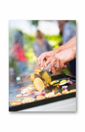 Close-up on hands grilling meat and vegetables on a plancha.