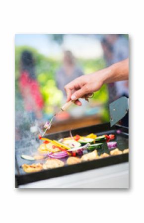 Close-up on hands grilling meat and vegetables on a plancha.