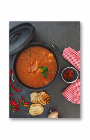 Spicy fish stew with tomatoes in cast iron pot with grilled bread slices on rustic table, top view