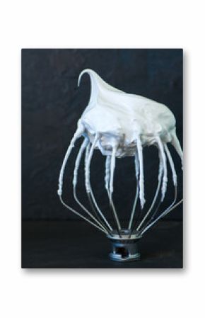 Whipped egg whites - beaten italian merengue on a whisk on black table,  closeup and copy space.