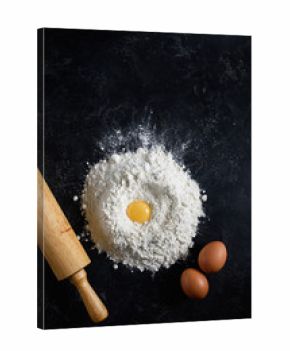 Flour, eggs and rolling pin on dark background. Top view. Baking ingredients. Bakery concept