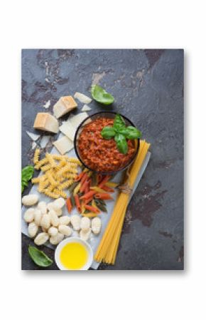 Above view of bolognese sauce with different types of raw pasta, gnocchi and other cooking ingredients, vertical shot with space