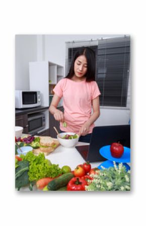 woman mixing salad while cooking with laptop in kitchen