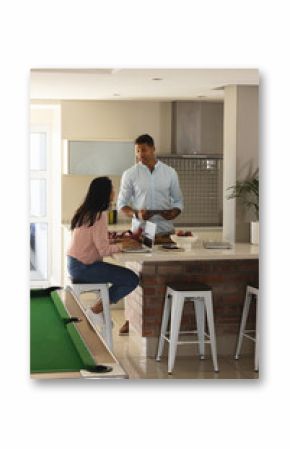 Diverse couple preparing breakfast in modern kitchen, chatting while using tablet and strawberries