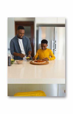 Making pizza together, African American father and son smiling in modern kitchen