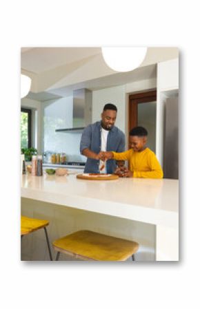African American father and son preparing meal together in modern kitchen, smiling