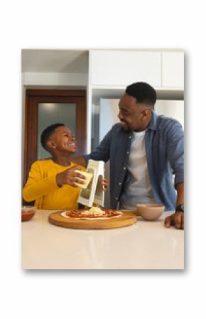Father and son making pizza together, grating cheese and sharing laugh