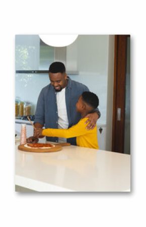 African American father and son making pizza in modern kitchen, using pizza dough and sauce
