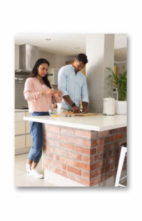 Preparing breakfast, couple cracking eggs and chopping vegetables in modern kitchen