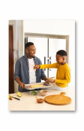 In kitchen, African American father and son preparing homemade pizza, smiling