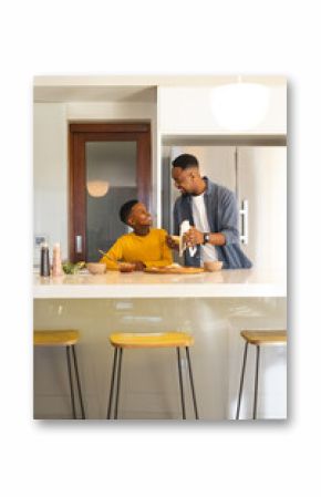 African American father and son preparing meal together in modern kitchen, smiling