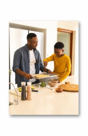 African American father and son preparing homemade pizza together in modern kitchen