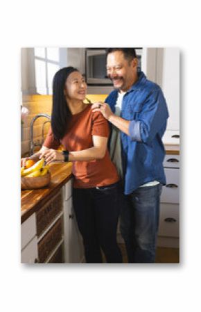 Mature Asian couple laughing together while preparing fresh fruit in cozy kitchen