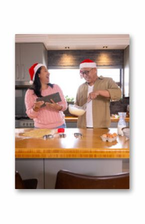 Christmas time, multiracial senior couple wearing santa hats baking, preparing treats, at home