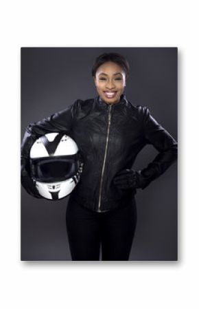 Black female motorcycle biker or race car driver or stuntwoman wearing leather racing suit and holding a protective helmet.  She is standing confidently in a studio