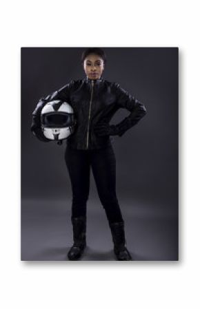 Black female motorcycle biker or race car driver or stuntwoman wearing leather racing suit and holding a protective helmet.  She is standing confidently in a studio