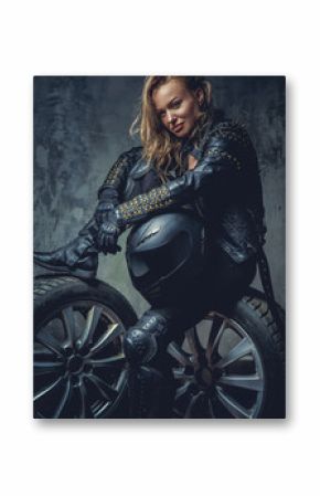 Blonde female in leather clothes sits on a car's wheel .