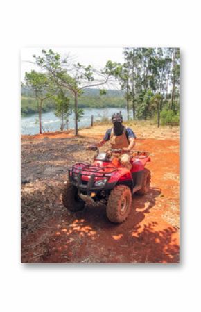 Man with kerchief on face sits on quad bike against Victoria Nile River background. Jinja, Uganda, Eastern Africa.   