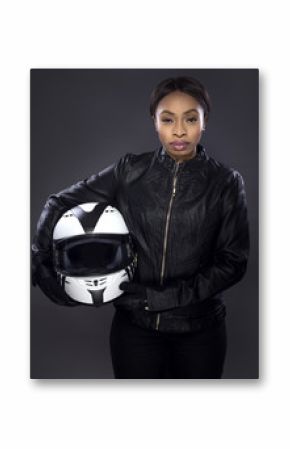 Black female motorcycle biker or race car driver or stuntwoman wearing leather racing suit and holding a protective helmet.  She is standing confidently in a studio