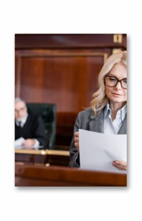 middle aged advocate in eyeglasses reading document while speaking in court