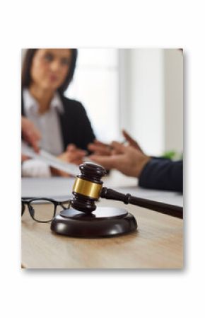 Close up of judge's gavel and glasses on table, with lawyer meeting with group of angry, complaining clients in background, giving legal advice, and helping with problem in court. Law services concept