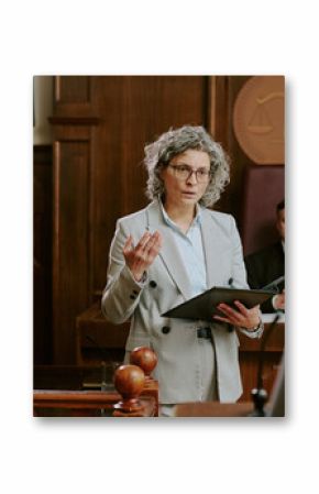 Caucasian middle aged woman lawyer addressing courtroom while holding folder, Caucasian teenage boy sitting at witness stand, judge and another woman present in background