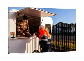 Young barrister serving older customer from coffee van on sunlit winter morning