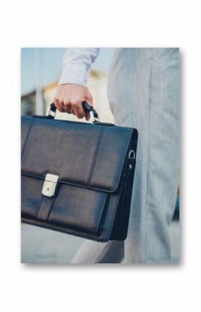 Confident business professional carrying leather briefcase in an urban cityscape during daylight, representing successful career.