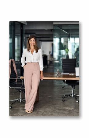 Happy professional elegant mature 45 years old business woman, smiling Latin businesswoman executive manager leader, middle aged female entrepreneur standing at work in office. Full body portrait.