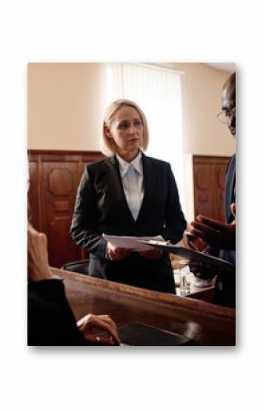 Defense and prosecution sides of court case standing in front of mature female judge while African American attorney explaining some points